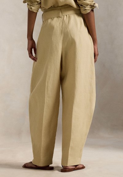 Λινές παντελόνες σε ανοιχτό μπεζ χρώμα, με φαρδιά γραμμή στο πόδι και εφαρμοστό ζωνάρι στη μέση. Φορεμένες με καφέ σανδάλια με επίπεδη σόλα.