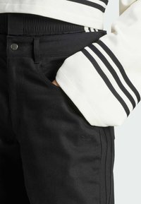 Los pantalones de denim negro cuentan con un ajuste ceñido, cintura elástica y un logo sutil. La modelo lleva una camiseta blanca con rayas negras.