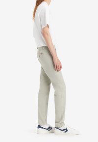 Jasnoszare dżinsy o dopasowanym kroju, z metką na tylnej kieszeni, zestawione z białą koszulą z krótkim rękawem i białymi trampkami.