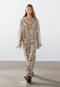 Pyžamo s leopardím vzorem v béžové a hnědé barvě, obsahující košili na knoflíky s dlouhými rukávy a kalhoty na šňůrku, vyrobené z měkké, lehké tkaniny.