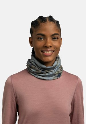 Young woman with braided hair wearing a light purple top and a blue-gray patterned neck gaiter, smiling against a plain background.