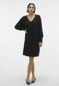 Abito nero lavorato a maglia con scollo a V e maniche lunghe, caratterizzato da una vestibilità ampia e polsini a coste. Texture liscia e design alla lunghezza del ginocchio.