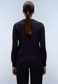 Zwarte longsleeve shirt in een losse fit, gemaakt van zacht materiaal. Heeft een ronde hals en geribde manchetten, gedragen met bijpassende zwarte broek.