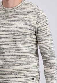 Bež pulover z nežnim sivim in črnim črtastim vzorcem, okroglim izrezom in rebrastimi manšetami. Mehka pletena tekstura z običajnim krojem.