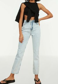 Svart crop top bärs med högmidjade ljusblå jeans. Jeansen har rak passform med en bleknad textur och en klassisk femfickorsdesign.