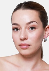 Orecchini a goccia in argento texture. Finitura liscia e lucida con una forma moderna, abbinati a un tono di pelle naturale e trucco minimale.