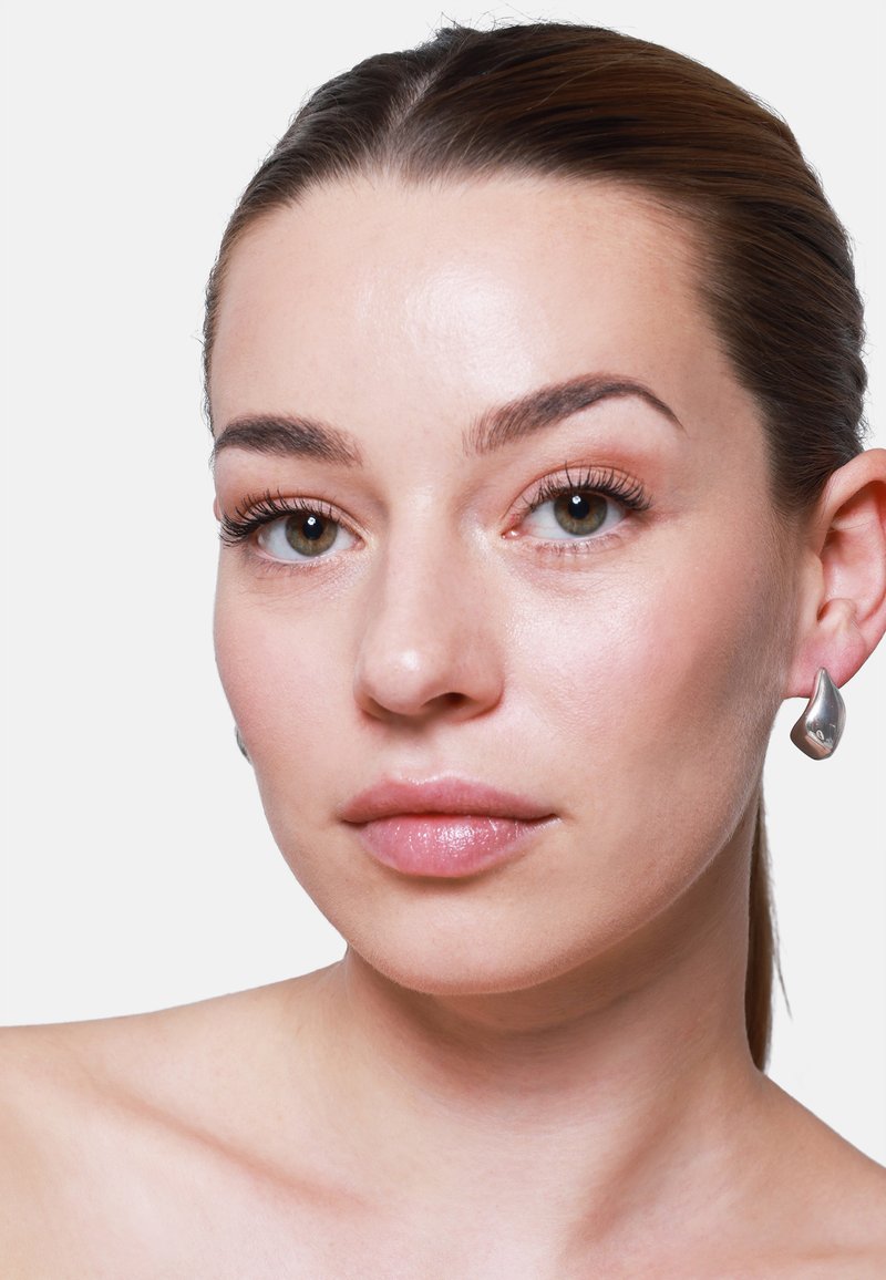 Orecchini a goccia in argento texture. Finitura liscia e lucida con una forma moderna, abbinati a un tono di pelle naturale e trucco minimale.