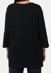 Texturerad marinblå topp med trekvartslång ärm, som har ett vågmönster och rund halsringning. Materialet verkar mjukt och lätt elastiskt.