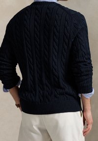 Navy blue knitted sweater with a cable pattern, ribbed cuffs, and hem. Worn over a light blue and white striped shirt.