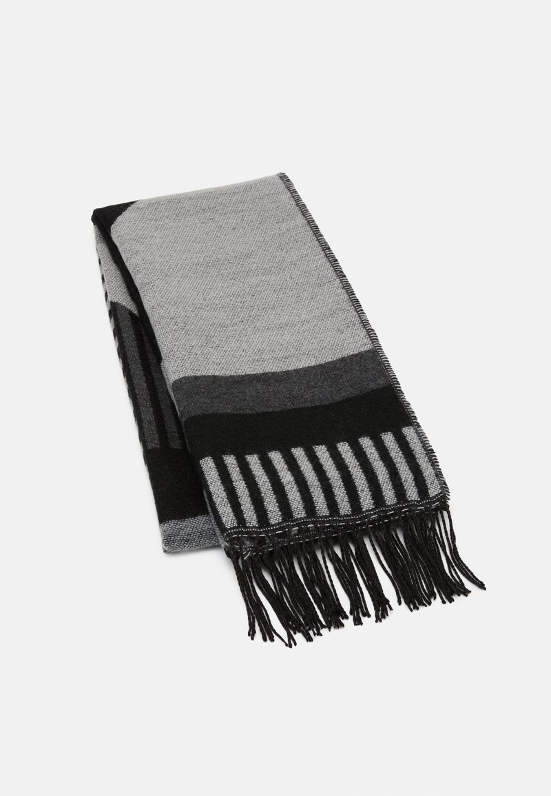 Écharpe pliée avec des motifs géométriques noirs et gris et des bords à franges sur fond blanc.