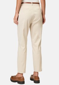 Pantaloni in cotone beige con vestibilità dritta, due tasche posteriori e una cintura in pelle marrone, abbinati a scarpe marroni slip-on.