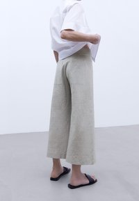 Lichtbeige wijde broek met een textuurafwerking, met een hoge taille en achterzakken. Gecombineerd met zwarte slip-on sandalen.