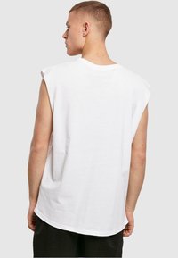 Hvid ærmeløs t-shirt lavet af bomuld med rund halsudskæring, i en afslappet pasform og glat tekstur med synlige syninger langs kanterne.