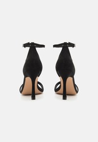 Musta mokkanahkainen korkokengät nilkkaremmillä, avonaisen varpaankohdan muotoilu ja hoikka stiletto-korko. Silkkinen beige pohja.