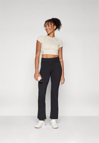 Lys beige cropped træningstop med korte ærmer, parret med sorte tætsiddende bukser. Model holder en vandflaske og har hvide sneakers på.