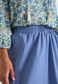 Falda azul a rayas con cintura elástica, combinada con una blusa de estampado floral que presenta flores verdes y azules, y detalles de borlas.