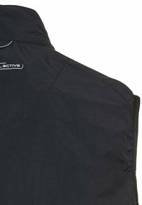 Czarna kurtka sportowa z wysokim kołnierzem, lekkim materiałem i zapięciem na zamek, z logo na górnej lewej stronie.