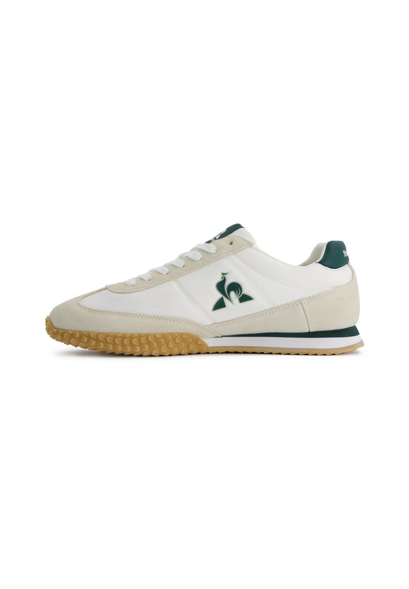 White and beige sneaker featuring a suede and leather upper, green accents, and a textured gum rubber sole with a sporty design.