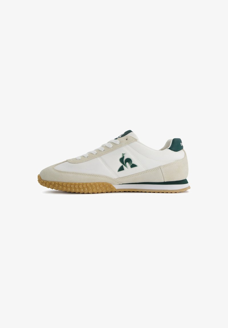 White and beige sneaker featuring a suede and leather upper, green accents, and a textured gum rubber sole with a sporty design.