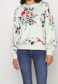 Vit sweatshirt med blommönster i rosa, röd och grön. Har ribbad muddar och nederkant, med rund halsringning och avslappnad passform.