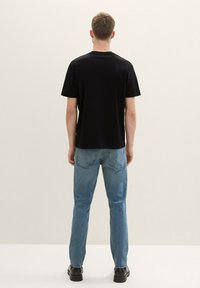 Tricou negru cu mânecă scurtă, din material de bumbac, croi lejer, combinat cu blugi albaștri deschiși și pantofi negri, văzut din spate.