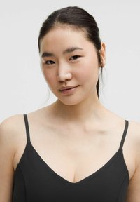 Black spaghetti strap top with a v-neck design, smooth texture, and fitted shape, resting on a light, neutral background.