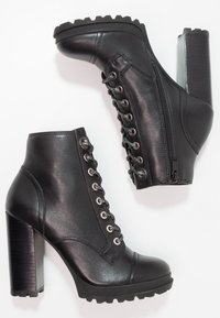 Botas de cuero negras hasta el tobillo con un alto tacón cuadrado, cordones en la parte delantera, cremallera lateral y suela texturizada. Presenta ojales metálicos y detalles de costura.