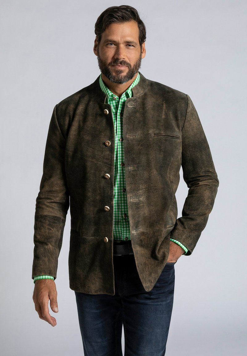 Chaquette de ante marrón con un cuello alto, cinco botones de latón y un bolsillo en el pecho, llevada sobre una camisa de cuadros verdes.