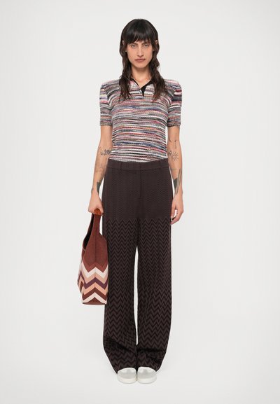 Polo w paski z krótkim rękawem, w połączeniu z szerokimi spodniami w czarno-białą zygzakowatą wzor. Trzyma torbę w wzór chevron.