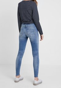 Smala blå jeans i blekt denim med normal hög midja. Bakfickor syns. Bärs med en svart- och vitrandig skjorta och vita sneakers.