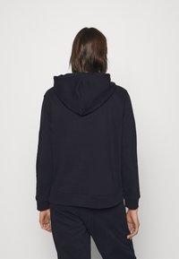 Sudadera con capucha de color azul marino, corte holgado, tejido suave, puños y dobladillo acanalados. Cuenta con un bolsillo tipo canguro en la parte delantera.