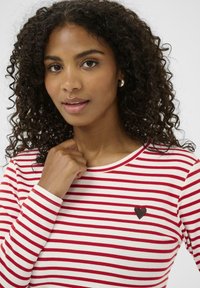 Červeno-biely pruhovaný top s dlhými rukávmi, okrúhlym výstrihom a malým čiernym srdiečkom vyšitým na hrudi. Mäkkučký materiál s rebrovanými manžetami.