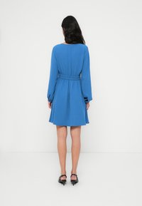 Μπλε  φόρεμα με μακριά μανίκια, εφαρμοστή μέση και φουσκωτή φούστα. Κατασκευασμένο από υφασμάτινη υφή, με στρογγυλή λαιμόκοψη και απλό σχέδιο.