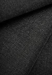 Black denim fabric with a textured weave, featuring a slight sheen and subtle flecks, folded over to show depth and softness.