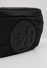 Sac en tissu matelassé noir avec un grand patch rond cousu sur le devant montrant un motif symétrique en forme de croix.