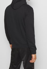 Felpa con cappuccio nera, dal tessuto morbido e polsini a coste, caratterizzata da un design semplice e una vestibilità rilassata, mostrata dal retro.