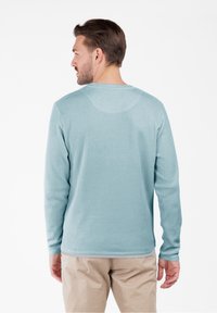 Top a maniche lunghe di colore azzurro chiaro, con texture, scollatura rotonda e polsini aderenti, abbinato a pantaloni beige. La vista dal retro mostra tutti i dettagli del design.