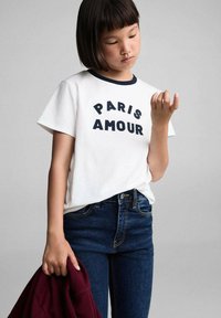 Bijela pamučna majica s tamnoplavim obrubom i natpisom "PARIS AMOUR" otisnutim na prsima. Uparena s tamnoplavim trapericama i bordo duksericom.