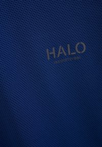 Blå nätliknande tyg med en strukturerad mönstring. Har logotypen "HALO" i mörkgrått, tillsammans med siffrorna "196819721981" nedanför.