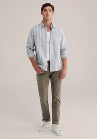 Svijetloplavi prugasti košulja na dugme uparen sa maslinasto zelenim hlačama i bijelim tenisicama; ležeran kroj, mekana tkanina i suptilni detalji.