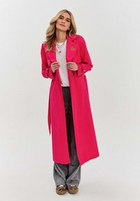 Fuksjowy trench coat z zapięciem na guziki i paskiem, noszony na białej bluzce i szarych spodniach w prążki, z dodatkiem butów w panterkę.