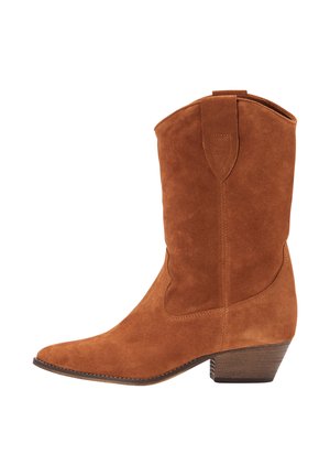 Ruskean npm-korkeaa cowboy-kenkää, jossa on kärki ja vetotappi, matala pinoon rakennettu puukorko, kuvattuna sivulta valkoista taustaa vasten.