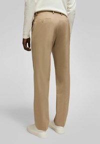 Beige op maat gemaakte broek met een gladde stoftextuur, voorzien van achterzakken en een rechte pijp, gedragen met witte sneakers.
