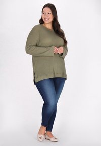 Olivgrön våffelstickad tröja med rundad halsringning, långa ärmar, sidofickor, ihop med blå skinny jeans och beige ballerinat. 
