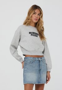 Felpa grigia cropped con testo nero "NO DRAMA PLEASE", abbinata a una gonna di jeans azzurri. Tessuto morbido, vestibilità rilassata e polsini standard.