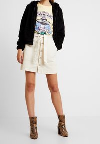 Svart fleece zip-up hoodie, gul t-shirt med UFO-motiv, beige knapprad kjol och bruna ormskinnseffekter ankelstövlar med klack.