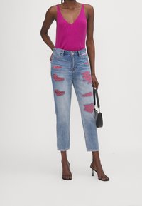 Upravený růžový tílko s ribem, popraskané svetle modré džíny s roztrhanými červenými záplaty a černé sandály na podpatku s pásky. Jednoduchá kabelka.