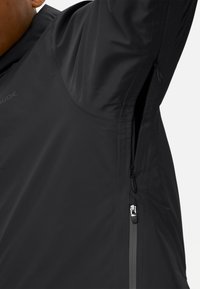Giacca nera con zip laterali, realizzata in materiale liscio e leggero. Presenta un design elegante e un colletto alto per una maggiore copertura.