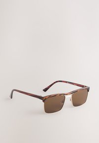 Occhiali da sole quadrati con lenti marroni sfumate, montatura con motivo tartarugato e dettagli dorati sul ponte. Design leggero con aste flessibili.