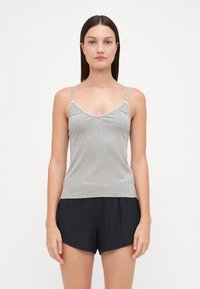 Top en maille grise avec des bretelles fines, présentant un décolleté en V et des bords festonnés. Porté avec un short noir à texture, ample.